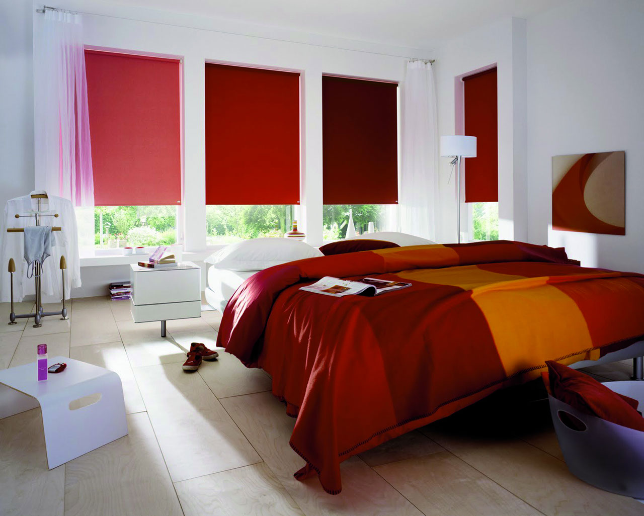 Chambre avec 4 fenêtres équipée de 4 stores écran à enrouleur. Ils sont chacun d'une couleur différente allant du rouge sombre à l'orange.