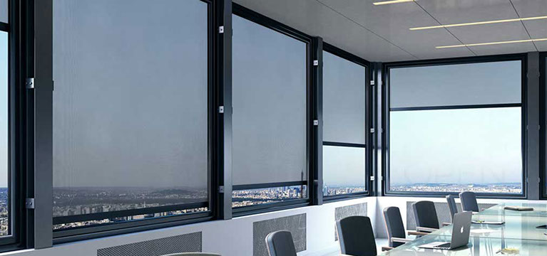 Angle salle de réunion dans un immeuble. Les fenêtres sont protégées par des stores films, verticaux guidés de couleur noire.